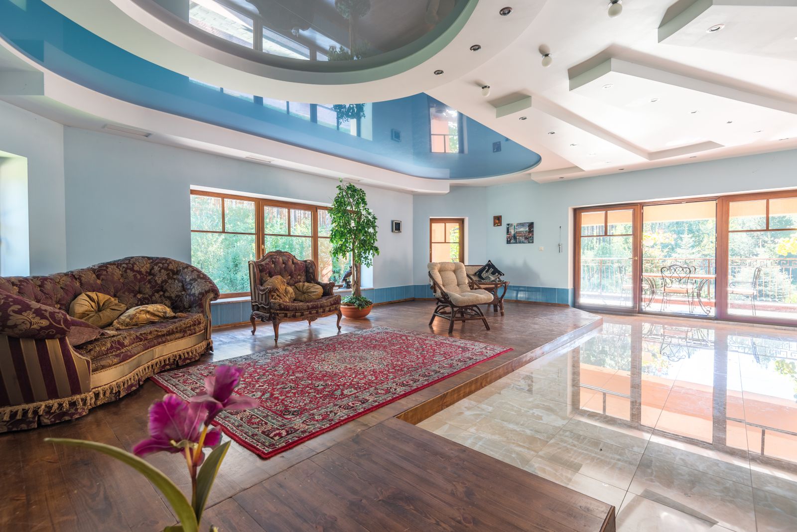 Spacious living room with a dramatic curved two-tone ceiling, tall windows, and a sitting area