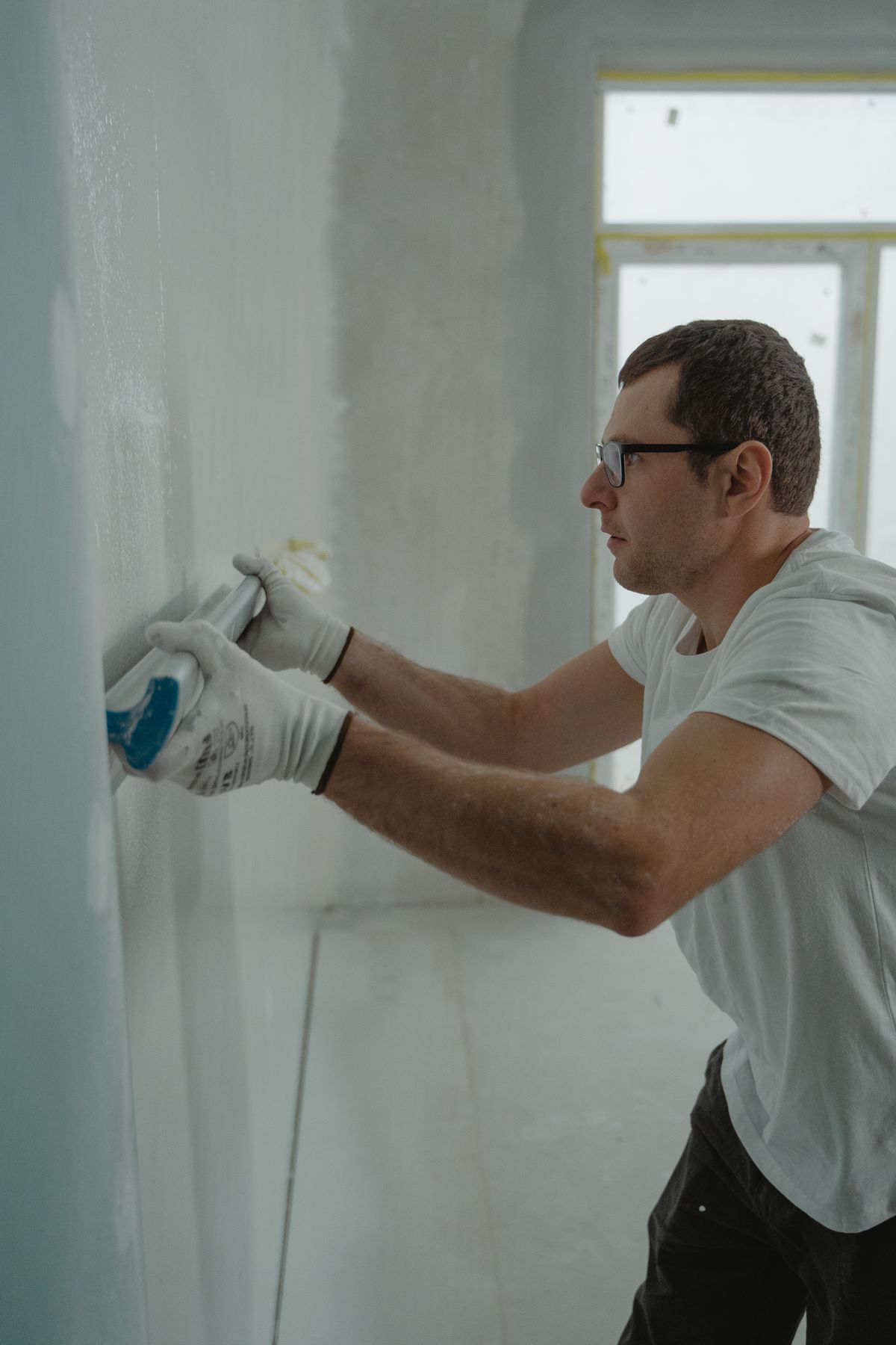 Worker in white gloves applying joint compound to a wall corner with a taping knife
