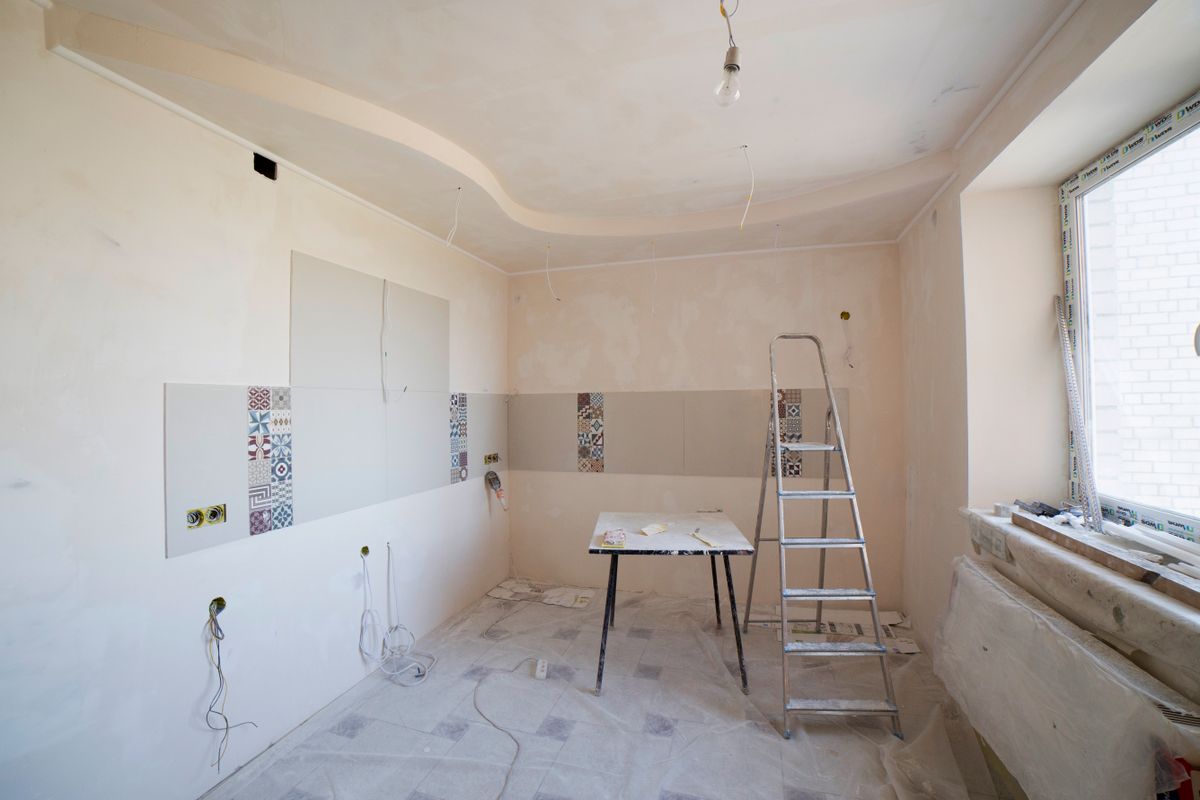 Kitchen mid-renovation with a stepladder, drop cloths on the floor, and a freshly finished stepped ceiling