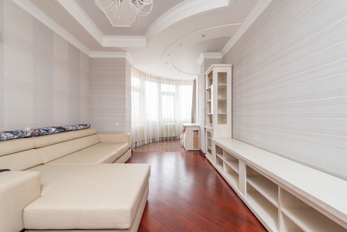 Long living room with a smooth white multi-level ceiling, recessed lighting, and a curved bay window